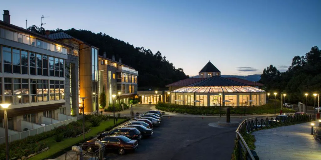 Vista nocturna del hotel balneario iluminado junto al pabellón acristalado, Lobios Caldaria