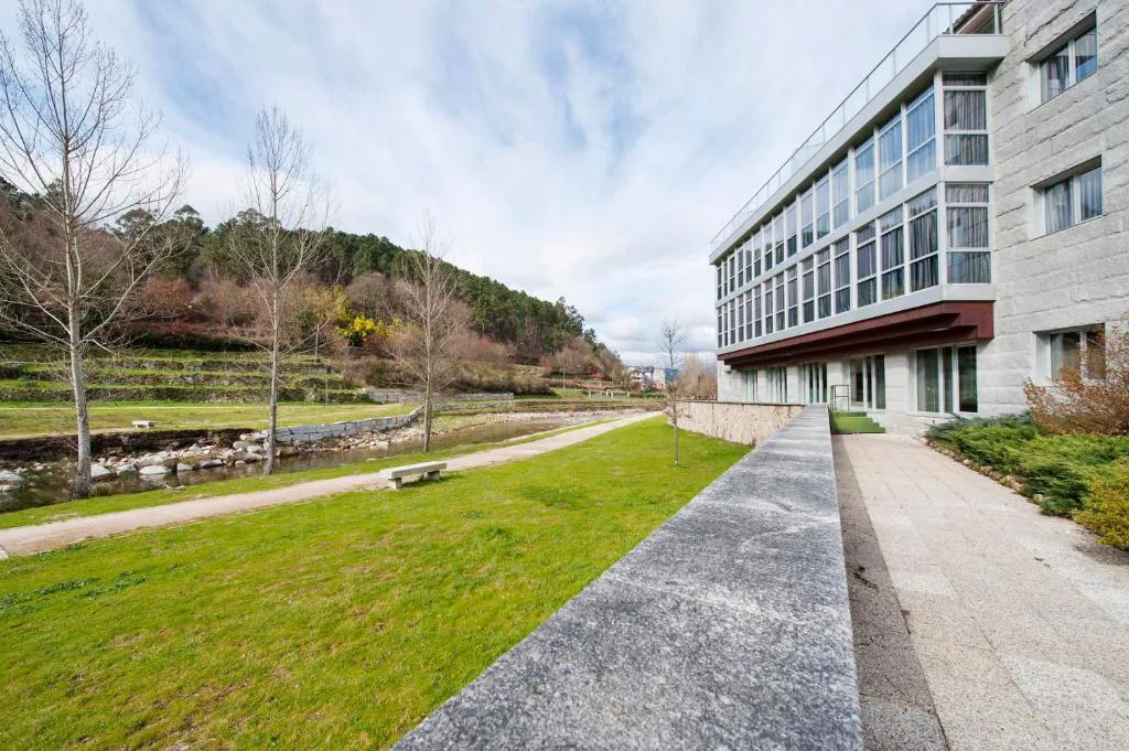 Fachada del hotel junto al río, con jardines y sendero, Lobios Caldaria