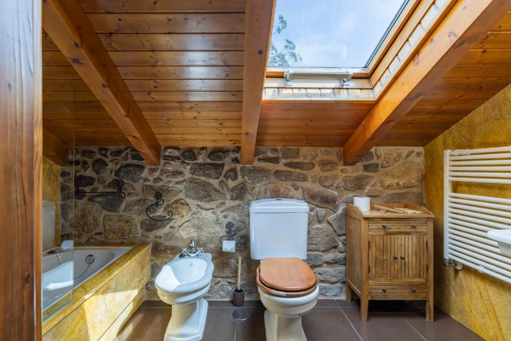 Baño abuhardillado de piedra con bañera de hidromasaje y claraboya, Lugar do Cotariño