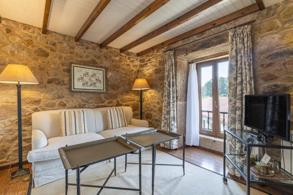 Salón con paredes de piedra vista, sofá y vigas de madera, Lugar do Cotariño