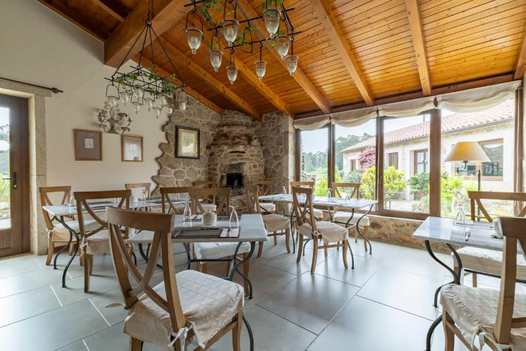 Comedor con chimenea de piedra y grandes ventanales al jardín, Lugar do Cotariño