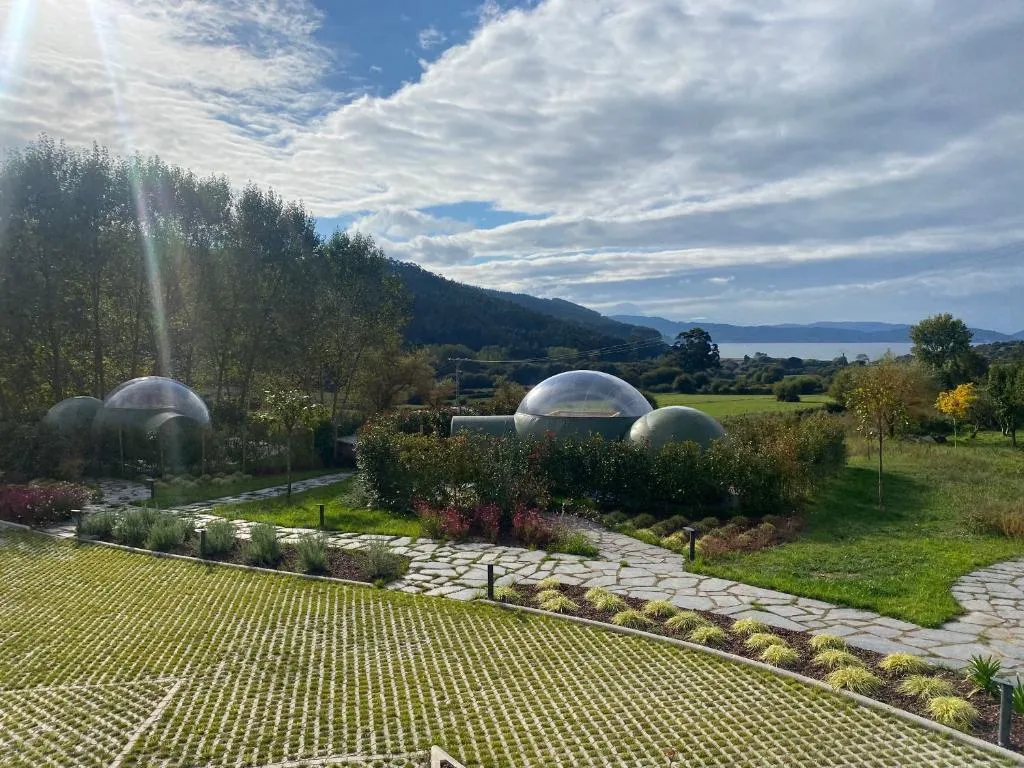 Vista aérea de las burbujas de Luzada Glamping entre jardines y el mar al fondo, en Xove, Lugo