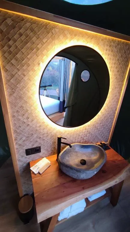Baño con lavabo de piedra y espejo circular iluminado en una burbuja de Luzada Glamping