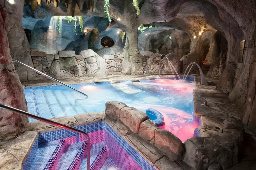 Cueva spa termal excavada en roca con piscina de hidromasaje e iluminación en tonos rosados, exclusiva para parejas