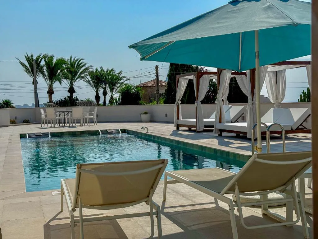 Piscina con tumbonas, sombrilla y camas balinesas