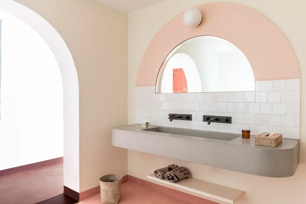 Baño con arco rosa, espejo circular y azulejos blancos, Menorca Experimental