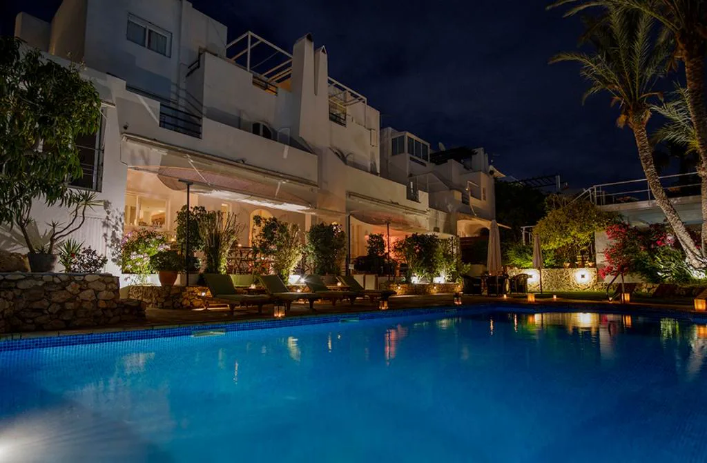 Piscina iluminada de noche junto a los edificios blancos del hotel