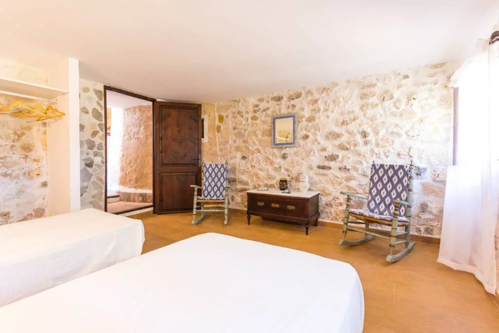 Dormitorio con mecedoras de estampado ibicenco junto a la pared de piedra, Molí D'en Barret
