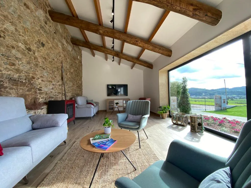 Salón de techos altos con pared de piedra, vigas de madera y ventanal panorámico al valle