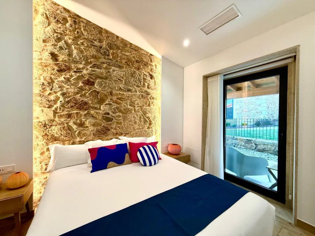 Dormitorio con cabecero de piedra iluminado y salida directa a terraza privada