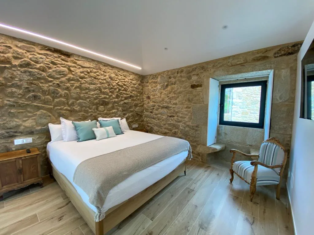 Segundo dormitorio de piedra vista con sillón de época junto a la ventana