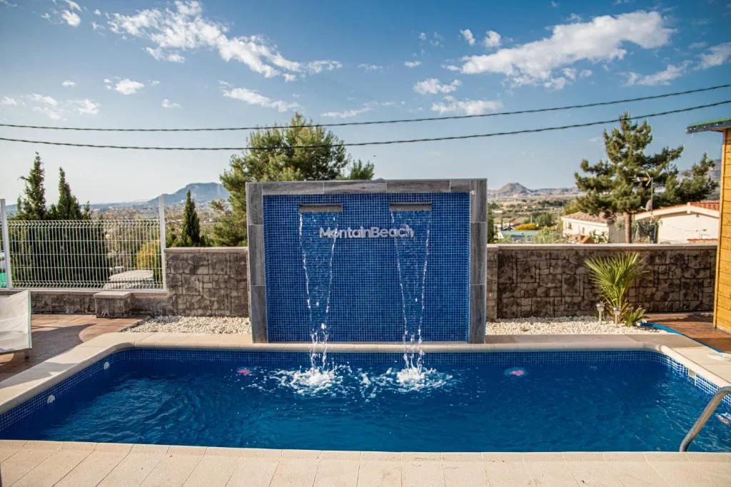 Piscina azul con fuente de agua junto a una pared de piedra