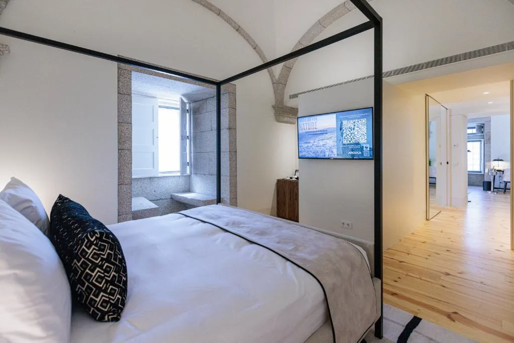 Cama con dosel bajo un arco de piedra original y ventana con poyete, MS Collection Arouca