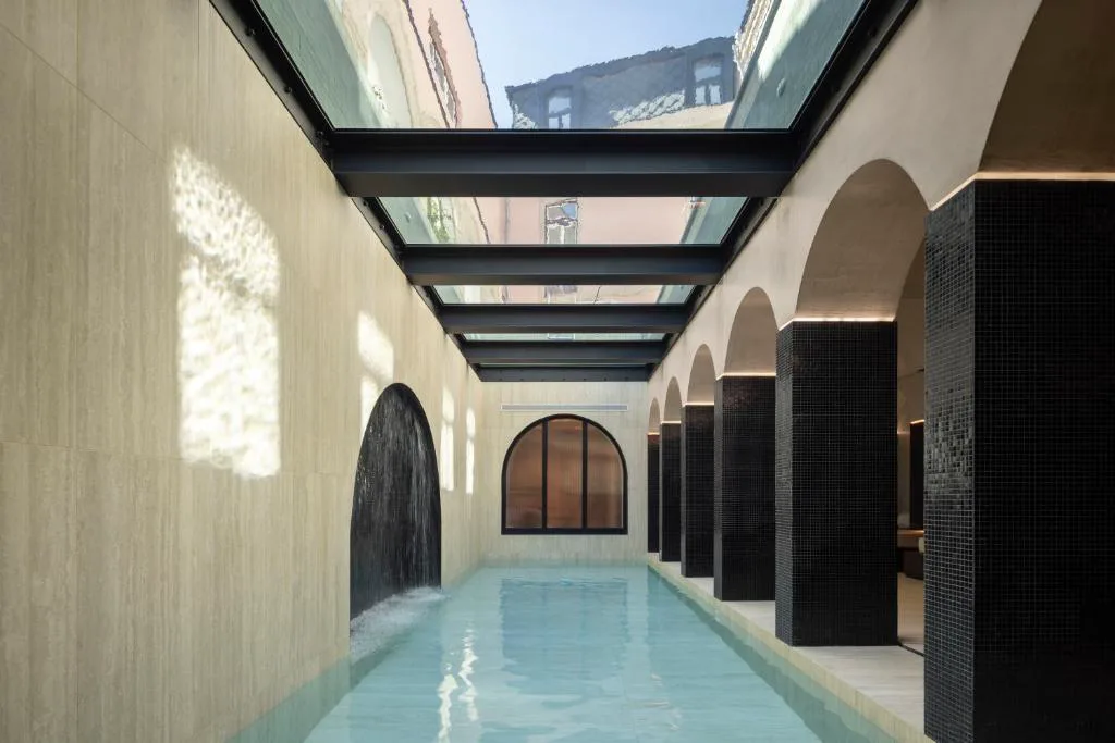 Piscina cubierta del spa bajo un techo acristalado entre arcos de piedra, Palacete Valdemouro