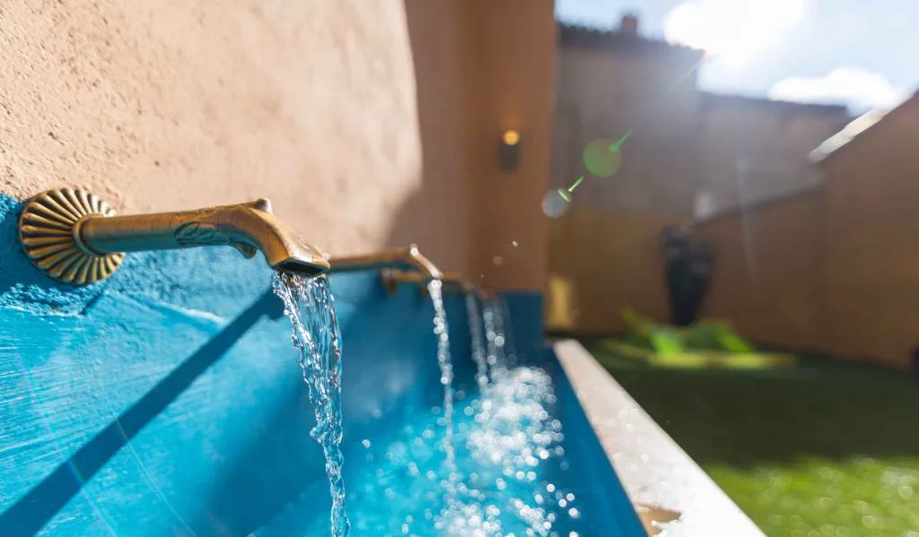 Piscina con cascada en un patio de paredes rojizas
