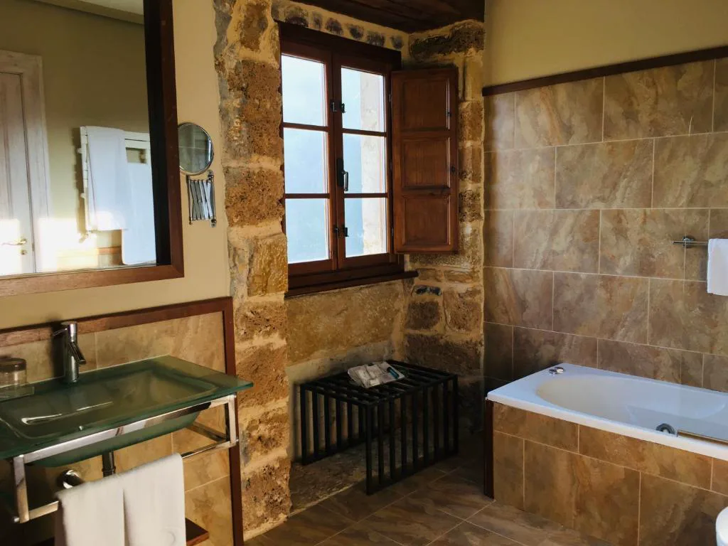 Baño de piedra con bañera de hidromasaje y lavabo de cristal