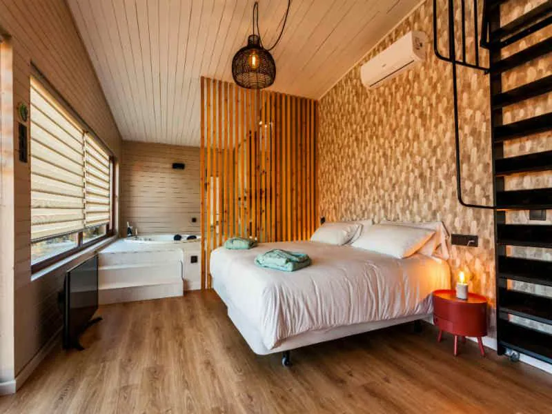 Suite con bañera de hidromasaje integrada junto a la cama, decoración de diseño en madera, Nidos de Carnota