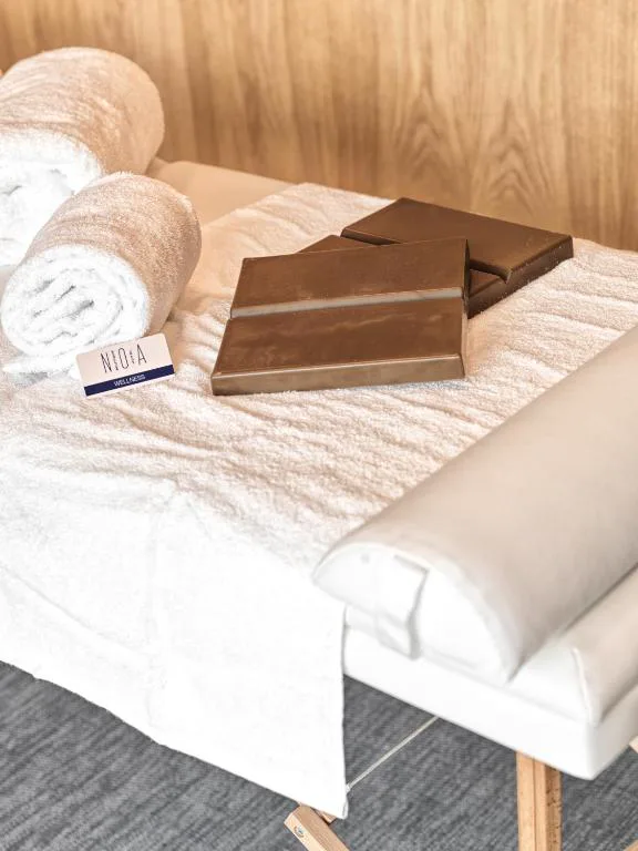 Detalle de bienestar con toallas enrolladas y chocolate sobre camilla de masaje, Noa Boutique Hotel