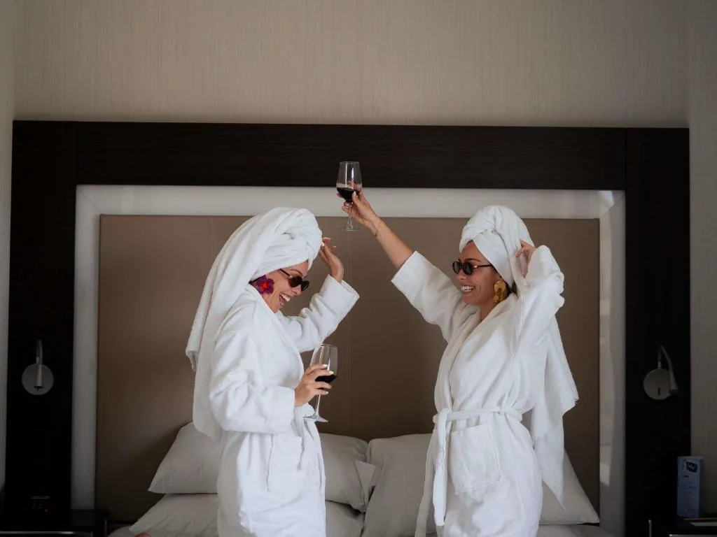 Dos personas con albornoces brindando en una habitación