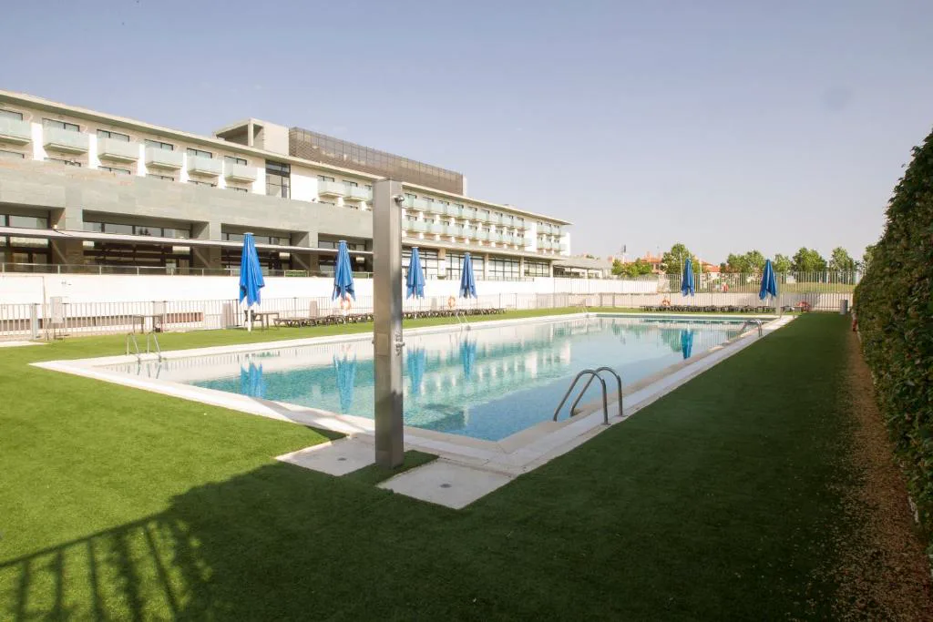 Piscina exterior alargada frente al hotel con césped