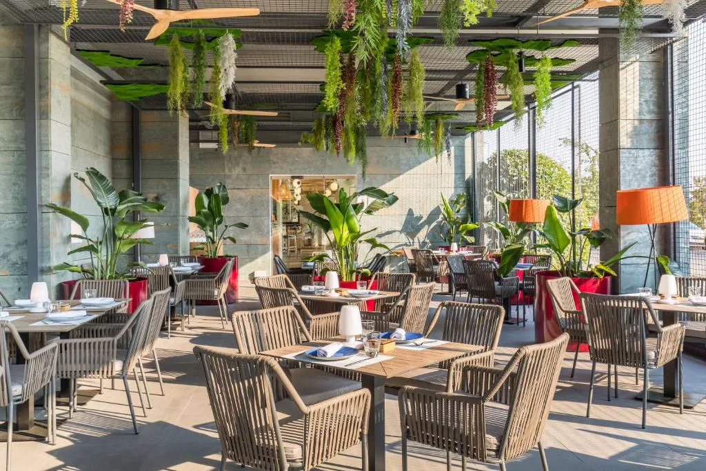 Comedor acristalado con plantas colgantes y mesas de mimbre