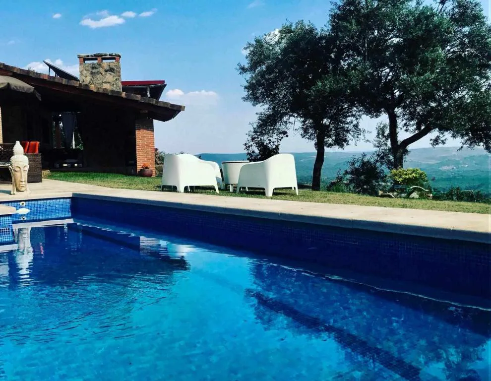 Piscina azul con tumbonas blancas frente a la casa de piedra y ladrillo y vistas al valle