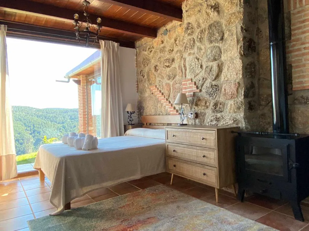 Dormitorio con muro de piedra, estufa negra y ventana al valle