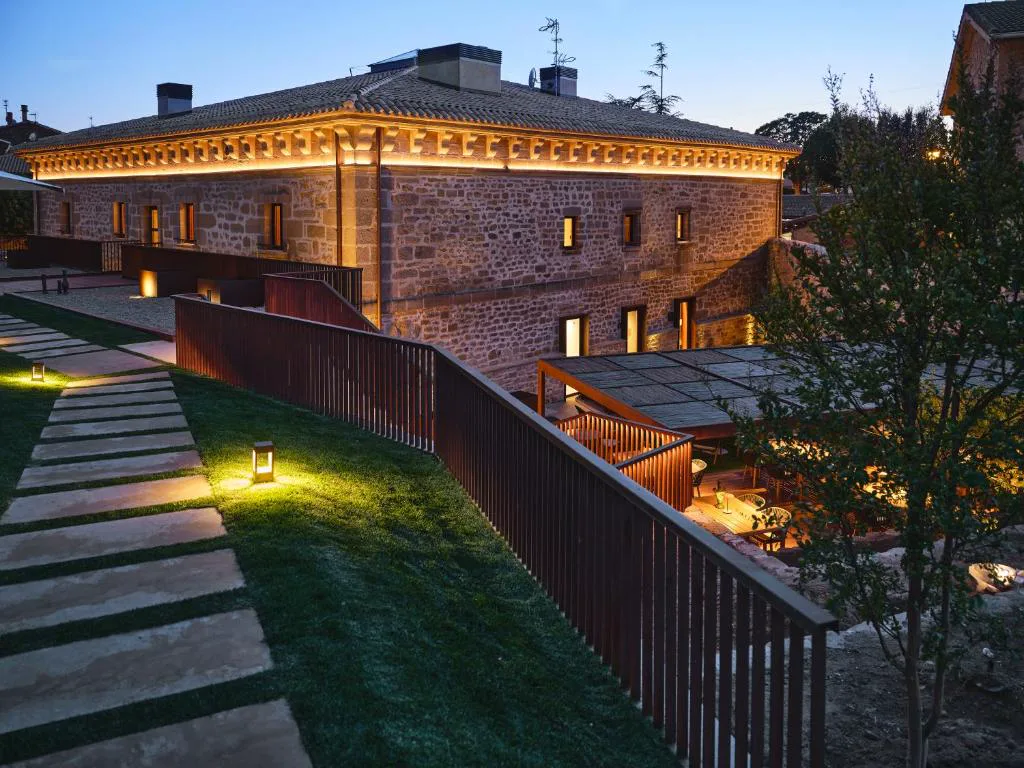 Edificio de piedra con pasarela y jardín iluminado