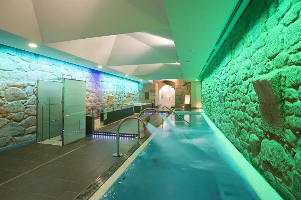 Piscina de spa integrada en los muros de piedra originales del monasterio, con iluminación verde, Parador de Santo Estevo