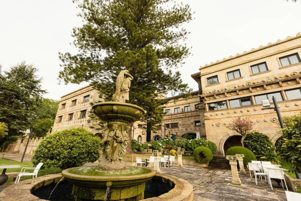Fuente de piedra tallada en el jardín, con el pazo histórico al fondo, Pazo Los Escudos