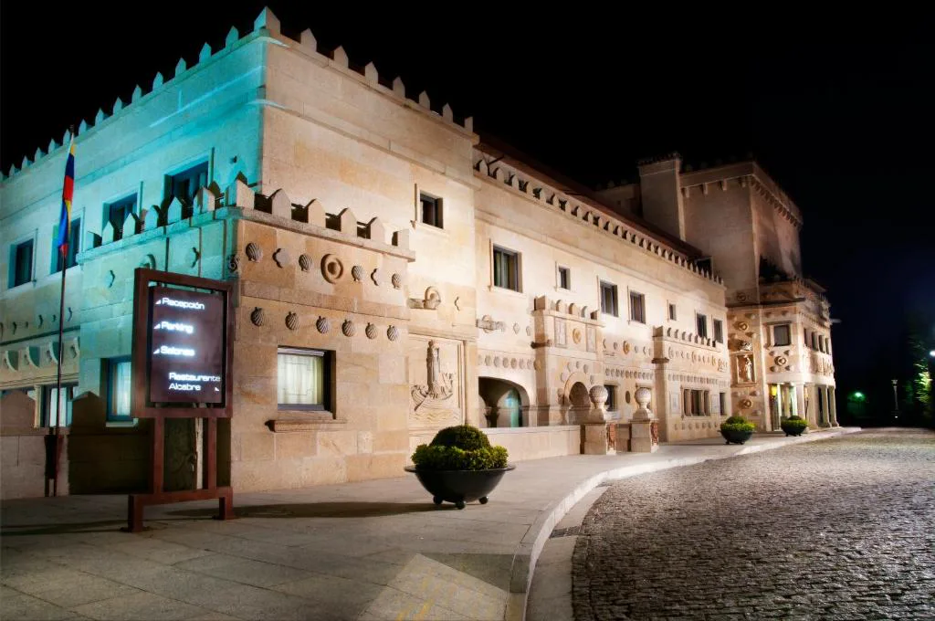 Fachada del pazo histórico iluminada de noche, con escudos de piedra tallados, Pazo Los Escudos