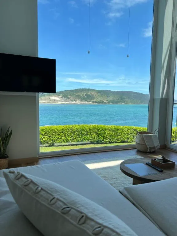 Salón con sofá blanco y ventanal panorámico frente al mar, Porto Cabana by Miramar Stays