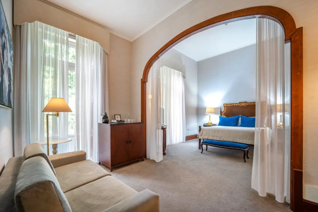 Suite con cama con dosel y cortinas blancas bajo arco de madera, Quinta das Lagrimas