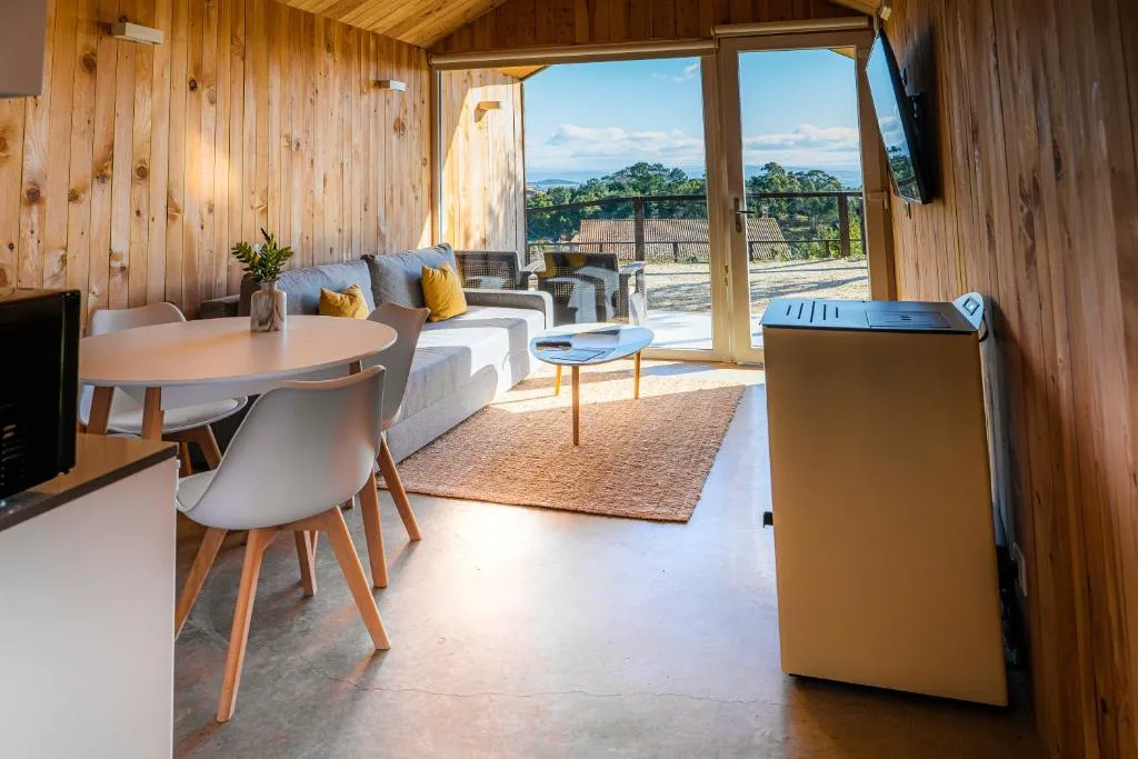 Salón comedor con mesa redonda y vistas al mar a través del gran ventanal, Cabañas Rías Baixas