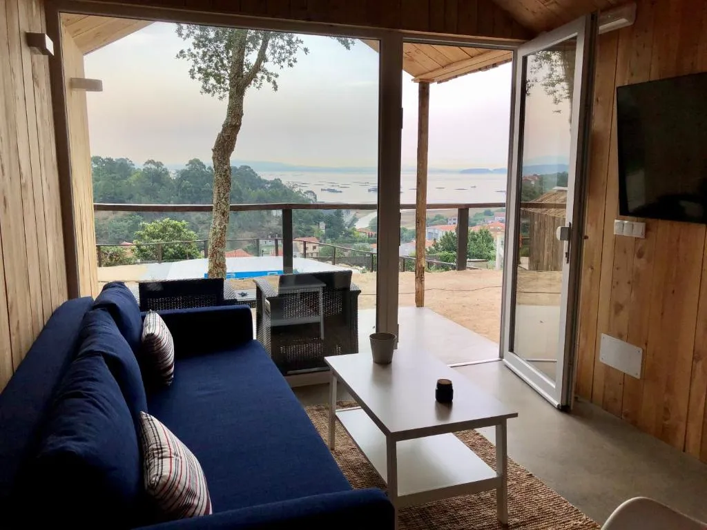 Sofá azul frente a un ventanal panorámico con vistas a la Ría de Arousa, Cabañas Rías Baixas