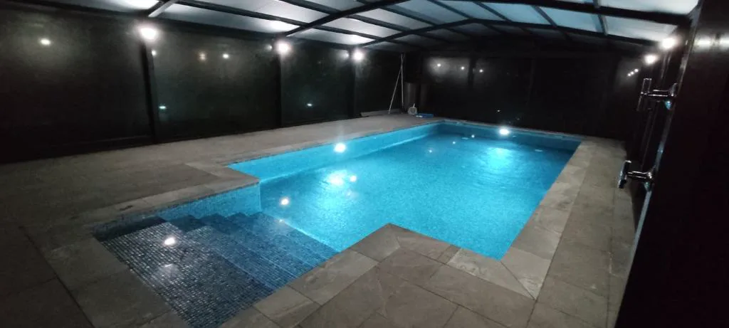 Piscina iluminada de noche bajo un porche con techo