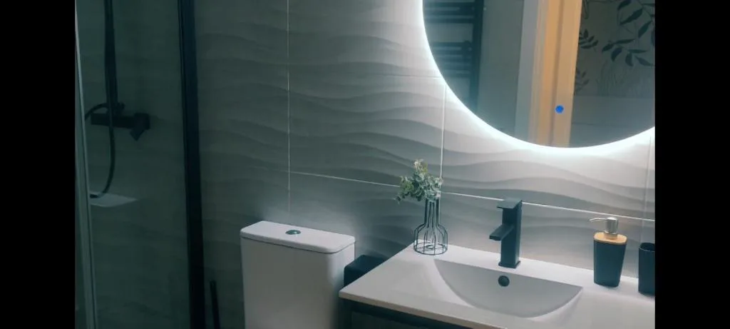 Baño con espejo redondo iluminado y ducha