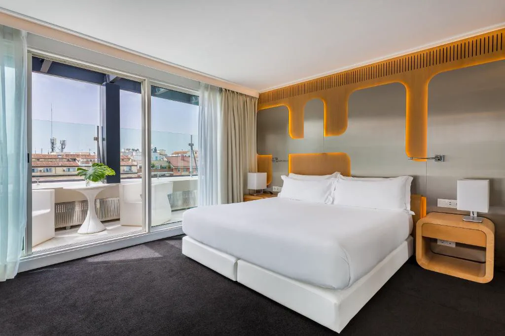 Habitación con cabecero amarillo y ventanal a la ciudad