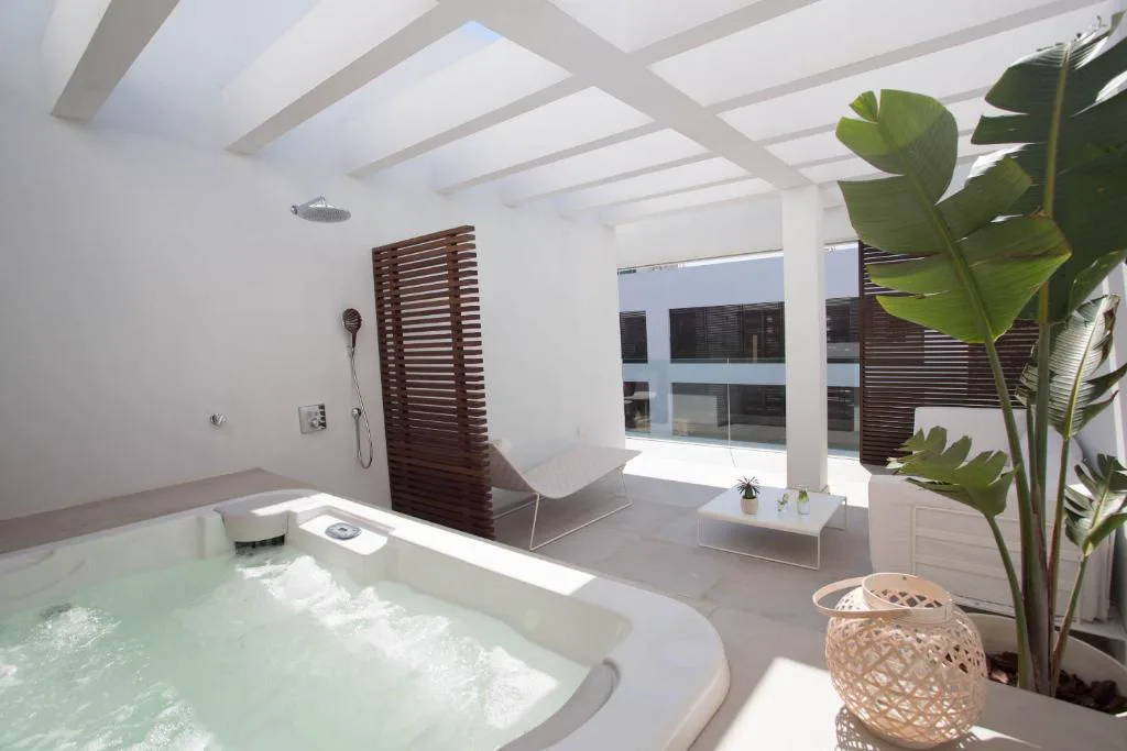 Bañera de hidromasaje burbujeante en terraza privada con planta de hojas grandes, Sa Pedrera Suites & Spa