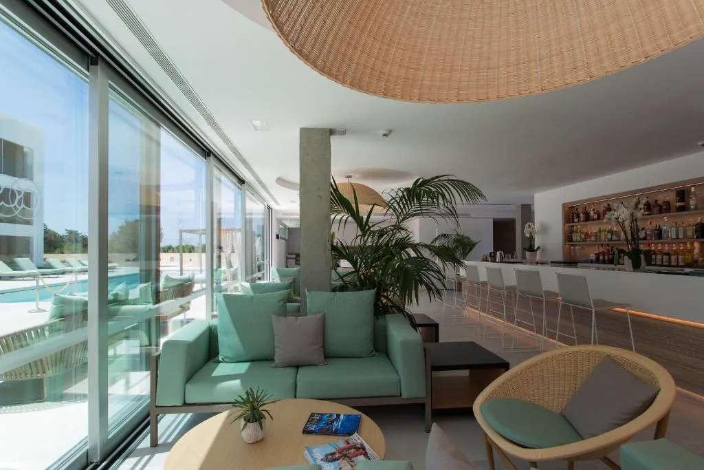 Salón bar con sofás verde menta y barra de copas junto a ventanales a la piscina, Sa Pedrera Suites & Spa