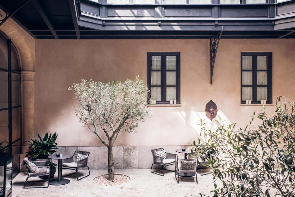Patio interior con olivo y mesas de hierro forjado junto a la fachada del palacete, Sant Francesc Hotel Singular