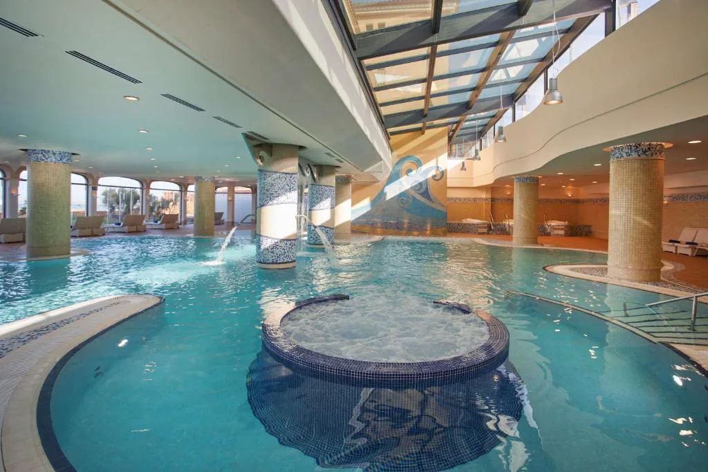 Piscina interior del spa con jacuzzi circular entre columnas de mosaico, Secrets Bahía Real
