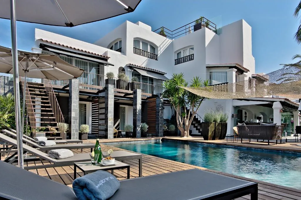 Fachada blanca mediterránea de Hotel Boutique Ses Pitreras con piscina y jardín de palmeras, en Sant Agustí des Vedrà, Ibiza
