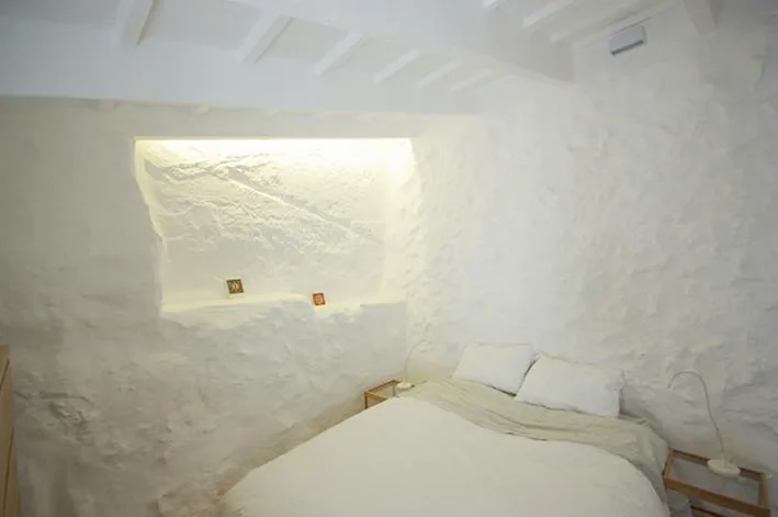 Dormitorio excavado en piedra encalada con luz natural, S'Olivera