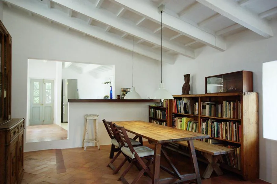 Comedor con mesa de madera maciza, librería antigua y vigas vistas, S'Olivera