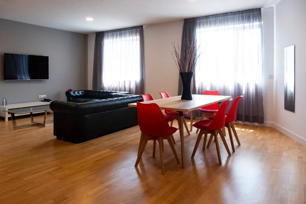 Salón moderno con sofá negro y sillas rojas, Spa Suites Odeón