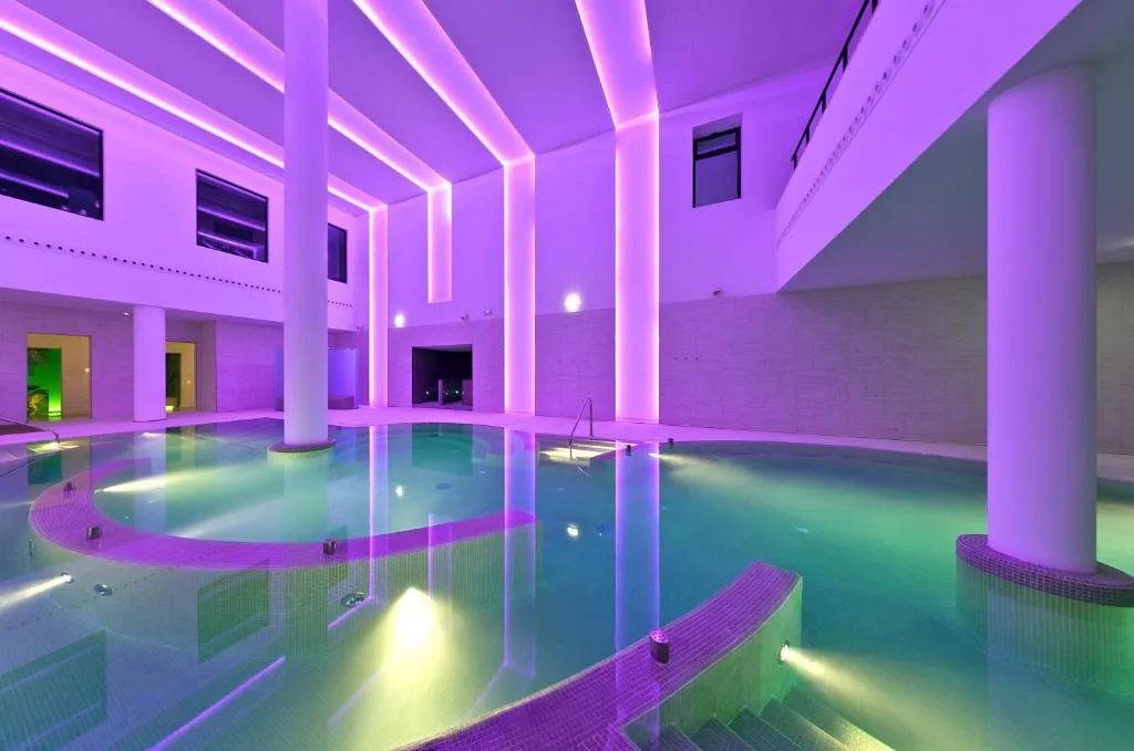 Piscina interior del spa con iluminación en tonos morados y columnas, Hotel Spa Zen Balagares