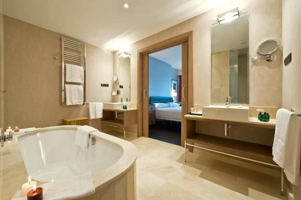 Baño con bañera exenta y vistas directas al dormitorio a través de un espejo panorámico