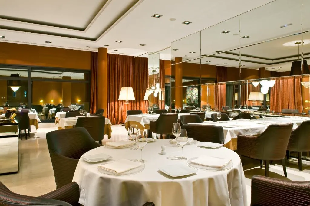 Restaurante del hotel con mesas redondas vestidas de blanco y cortinas en tonos cobrizos