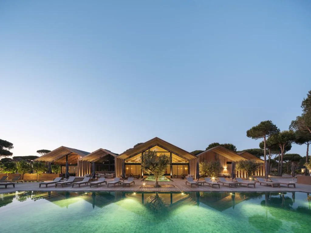Piscina de Sublime Comporta iluminada al anochecer, entre las villas de madera